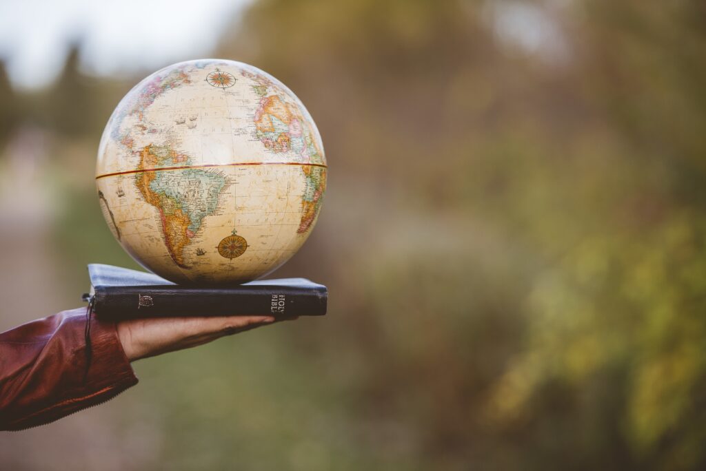 closeup shot of a person holding bible with desk globe on top with a blurred background
